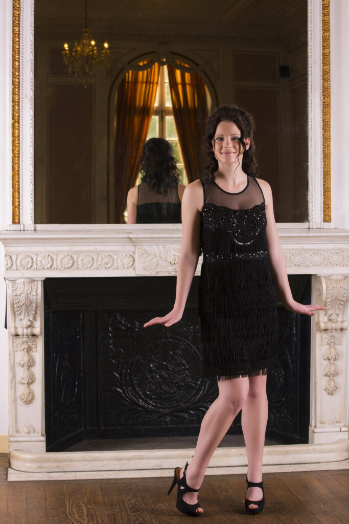 young lady in a black dress by a fireplace